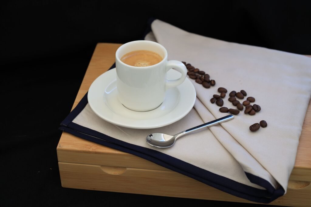 A close-up of an espresso cup on a wooden tray with scattered coffee beans and a teaspoon.